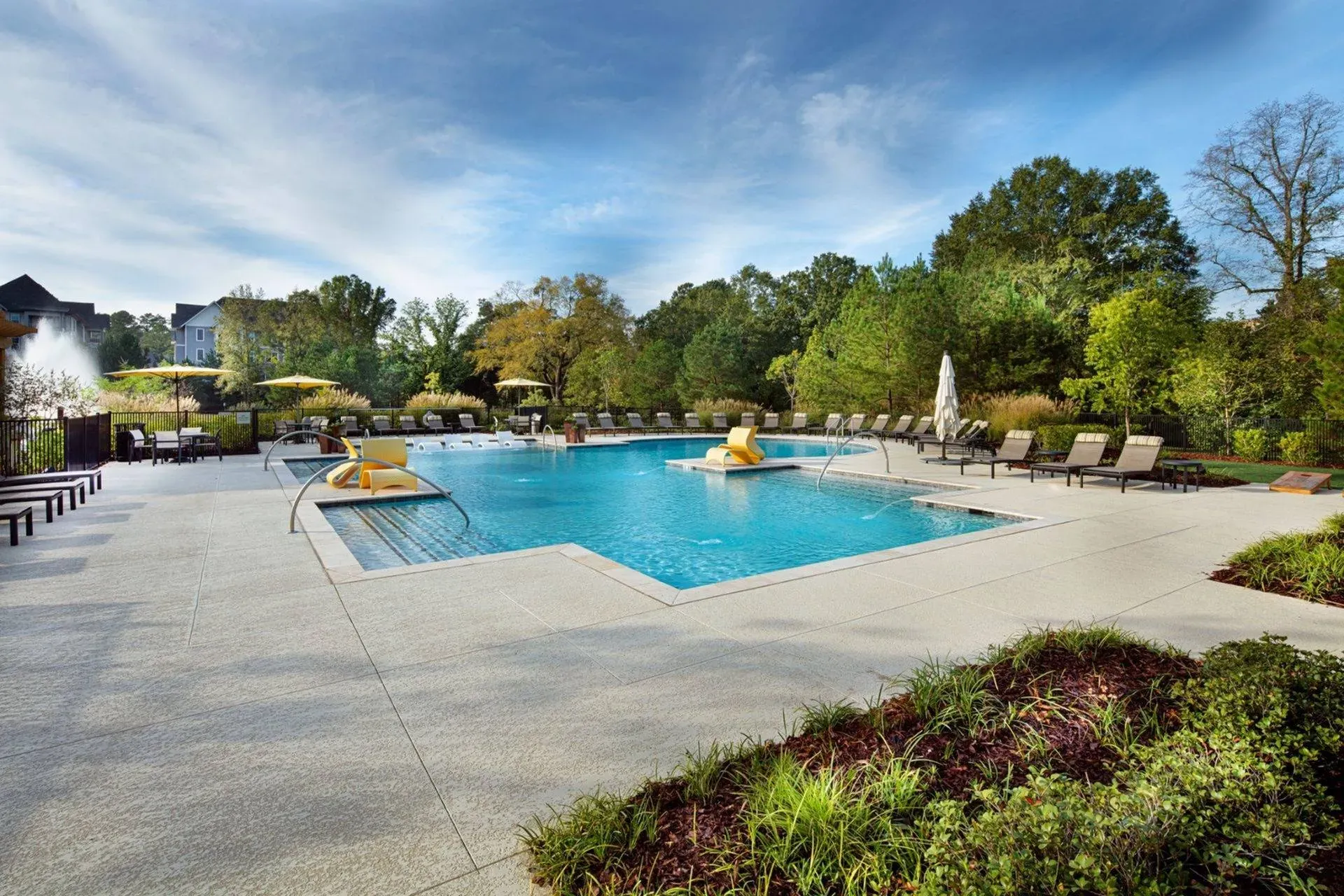 Vestavia Reserve Outdoor pool with lounge chairs and umbrellas, surrounded by greenery under a partly cloudy sky.