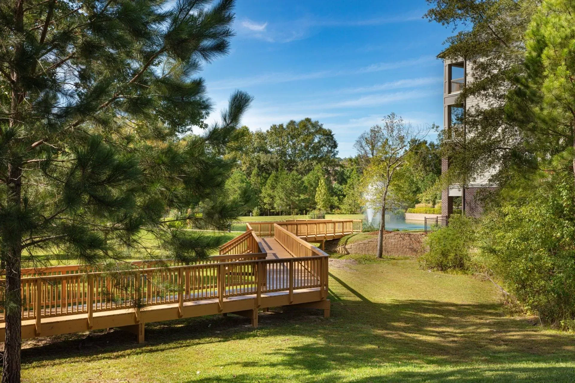 Vestavia Reserve Wooden boardwalk in a park with trees and a pond, under a clear blue sky. A building is visible in the background.